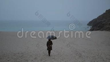一个带着雨伞的孤独女人沿着海滩走到海滨。